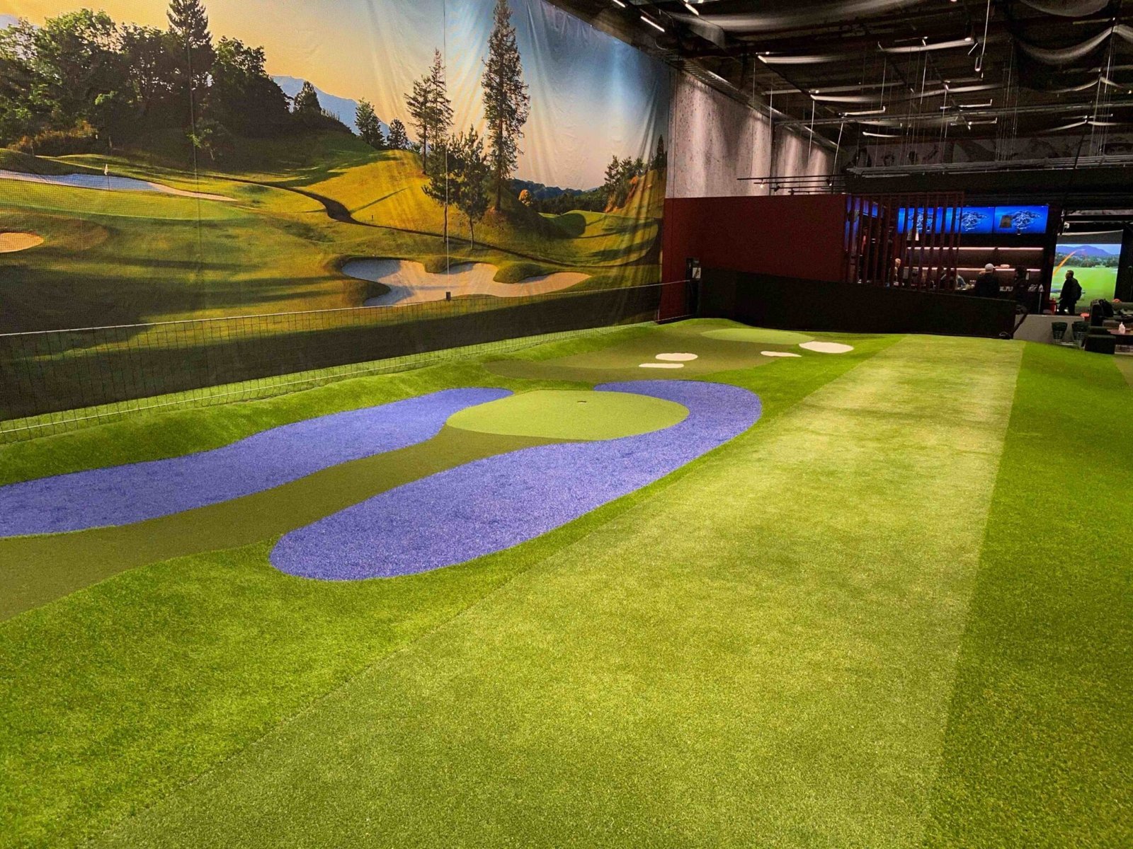 GoGolf Loungen sisähalli: vihreää ja sinistä tekonurmea golfkenttämaalauksen edessä.